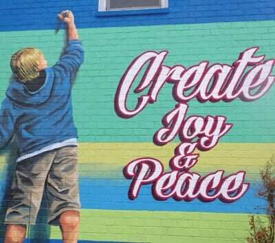 painting on brick of a boy drawing saying "Create Joy and Peace"