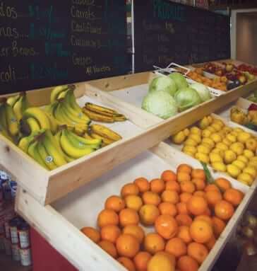 Insdie a fruit stand showing fresh bananas, oranges, lemons, lettuce, etc.