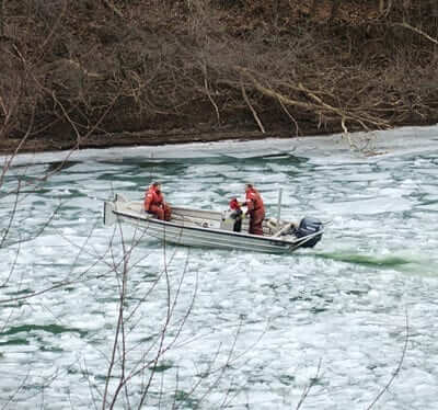 Three men wearing life vests on a motorboat on an ice covered river