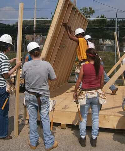 Women lifting up a wall to help build a house