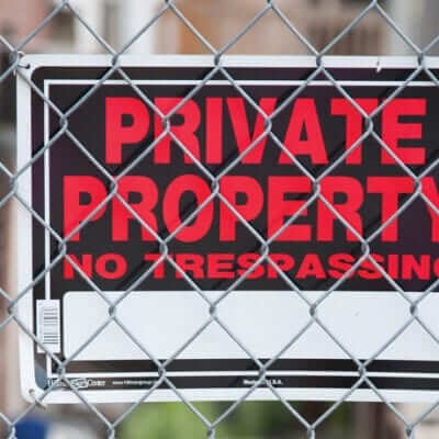 Sign hooked behind a fence that reads " Private Property No Trespassing"